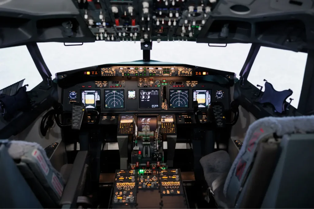 Panel de instrumentos y asientos en la cabina de mando iluminada de un avión comercial moderno.