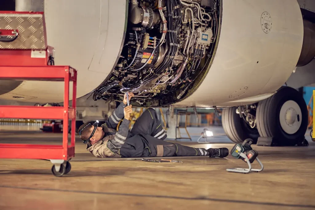 Mecánico de aviación trabajando tumbado bajo el motor abierto de un avión comercial en un hangar.